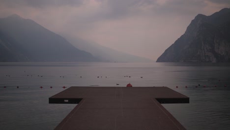 wooden pier in riva del garda beach, with garda lake and mountains on background