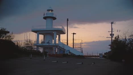 Picturesque-lighthouse-in-Saikazaki,-Japan,-stands-against-the-backdrop-of-a-golden-hour-sunset-sky,-creating-a-serene-evening-scene