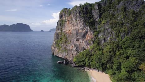 aerial pedestal up on huge limestone cliff tilting down on beautiful sandy beach in el nido, palawan, the philippines