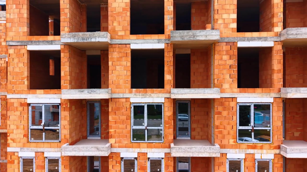 Primer plano de la fachada de ladrillo de un edificio residencial. Vista frontal de la fachada de una casa de varios pisos sin terminar, hecha de bloques de arcilla naranja con ventanas instaladas.