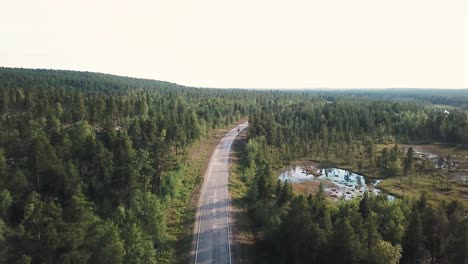 Forward-drone-shot-over-motorcyclist-riding-a-road-inside-a-forest-in-north-Finland,-Europe,-above-the-arctic-circle