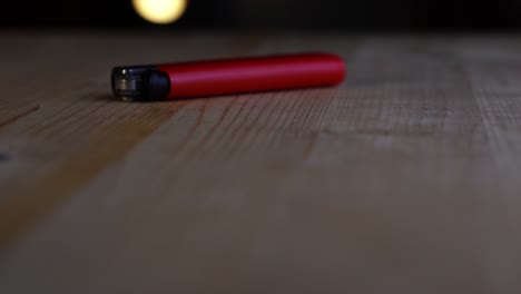 red lighter with a black cap lies on a light wooden table and slowly rotates