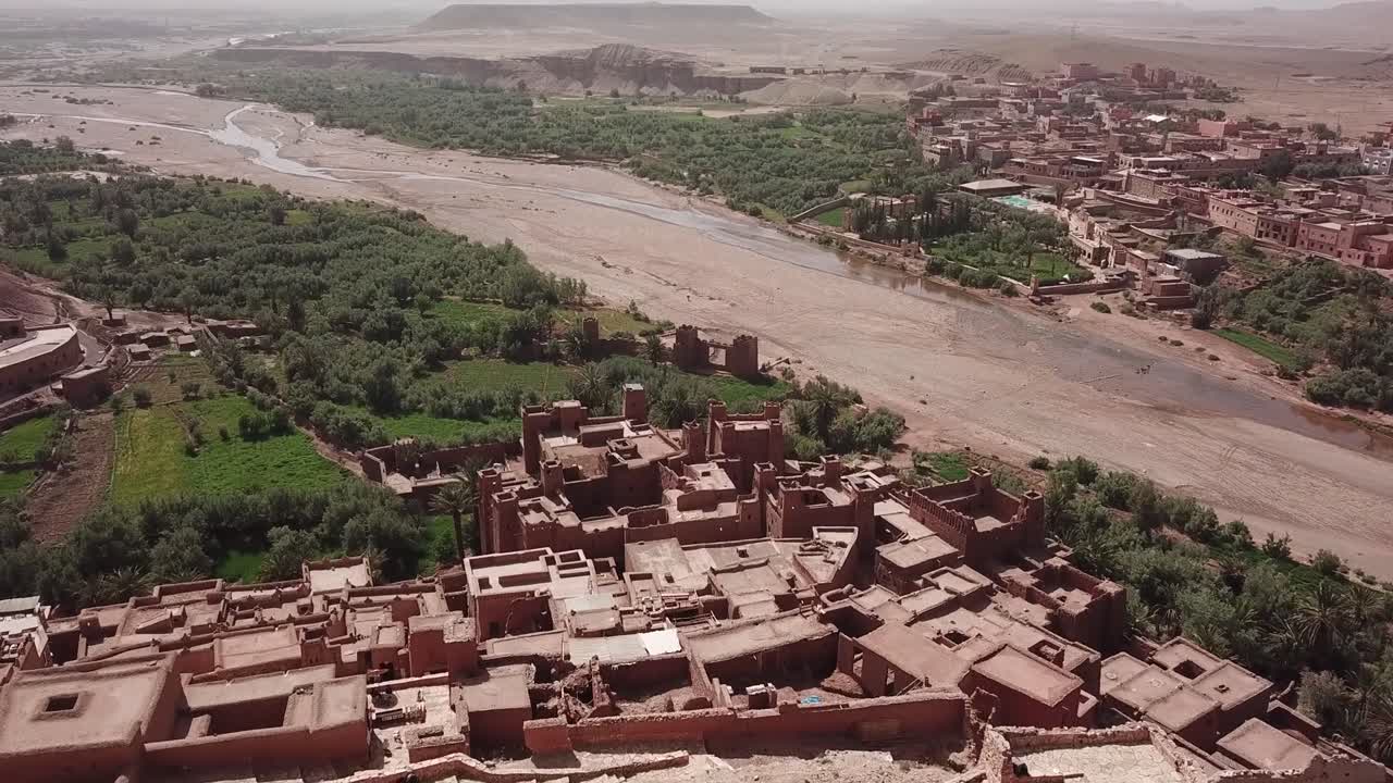 Góc nhìn từ drone về một tháp kasbah nhìn ra thung lũng ốc đảo rộng lớn và lòng sông khô cạn gần Ait Benhaddou ở Ouarzazate. Sự tương phản mạnh mẽ giữa cao nguyên sa mạc và cảnh quan màu mỡ, lý tưởng cho du lịch và điện ảnh