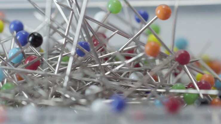 Close up of colorful sewing pins with round heads stored in transparent plastic container, macro shot