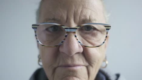 caucasian woman wears colorful transparent glasses staring shot closeup at camera, senior lady with white hair, looks closely, portrait face