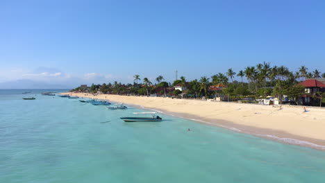 Nusa-Lambogan-Wunderschöner-Sonnenuntergangsstrand-Mit-Kristallklarem-Meer-Und-Weißem-Sand,-Segelbooten-Und-Palmen