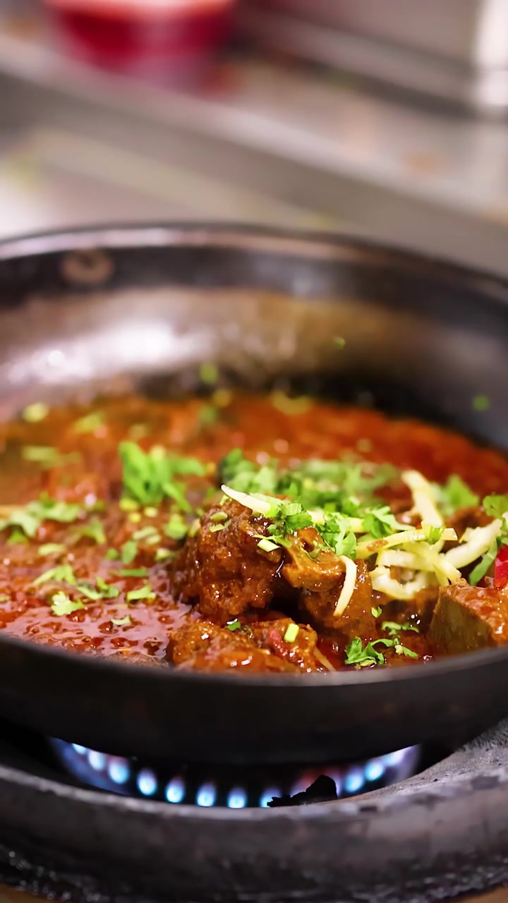 Primo piano di curry di carne che sobbolle sul fornello a gas mentre lo chef spruzza guarnizione di coriandolo fresco