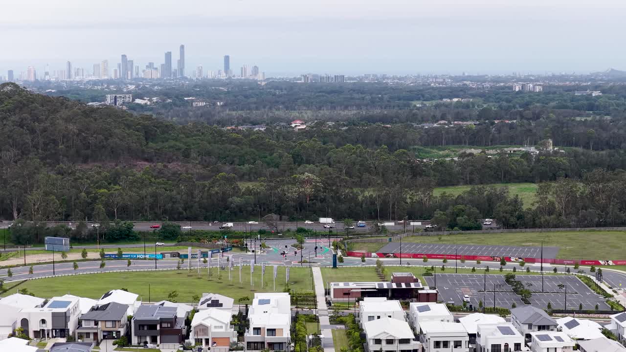 Drone camera glides over modern suburban homes toward city skyline, overcast daylight, wide perspective