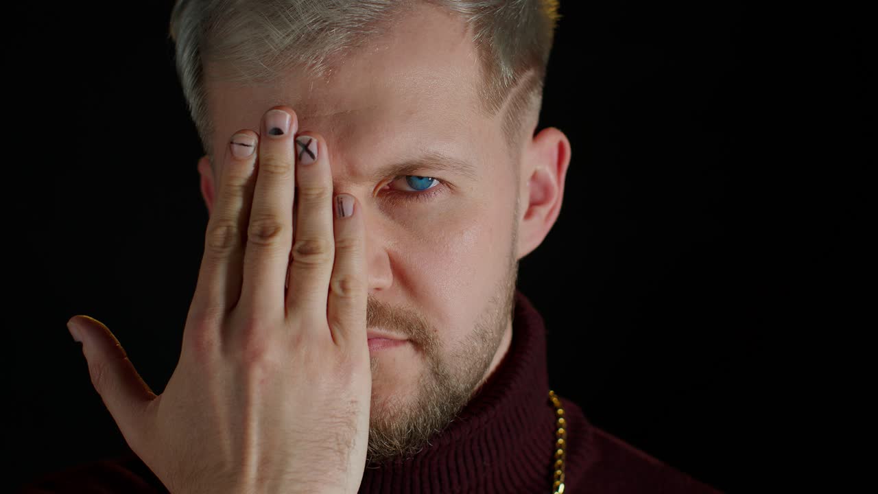 자신감 넘치는 스타일리시한 수염이 있는 남자가 한쪽 눈으로 카메라를 감각적으로 바라보고, 포즈를 취하고, 얼굴 표정을 하고