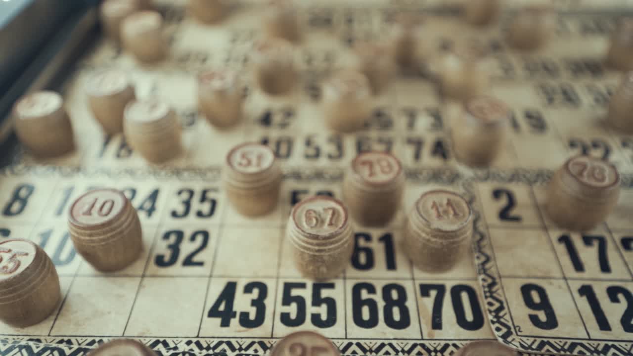 video macro de un tablero de bingo, luces de estudio, 120 fps, cámara lenta, dígitos de chips de madera, imágenes en bruto, juego de mesa de lotería, números de cartas, grúa tirando hacia atrás movimiento suave, disparado desde arriba