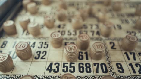 video macro de un tablero de bingo, luces de estudio, 120 fps, cámara lenta, dígitos de chips de madera, imágenes en bruto, juego de mesa de lotería, números de cartas, grúa tirando hacia atrás movimiento suave, disparado desde arriba