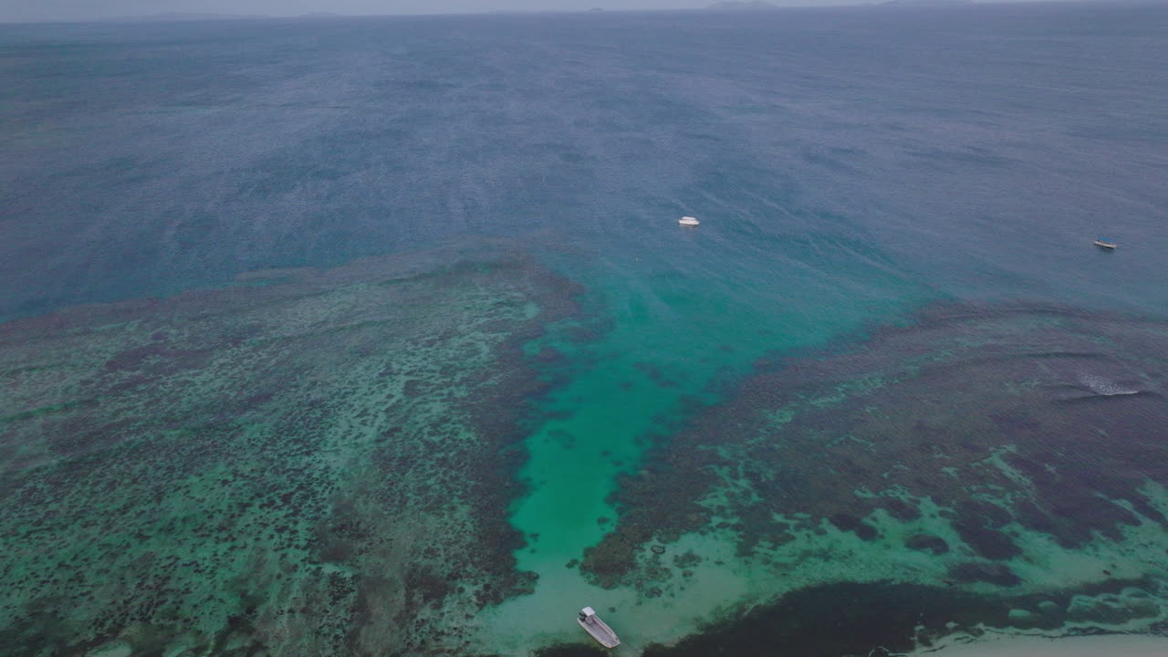Overhead drone of coral reef and boat navigating near island coast