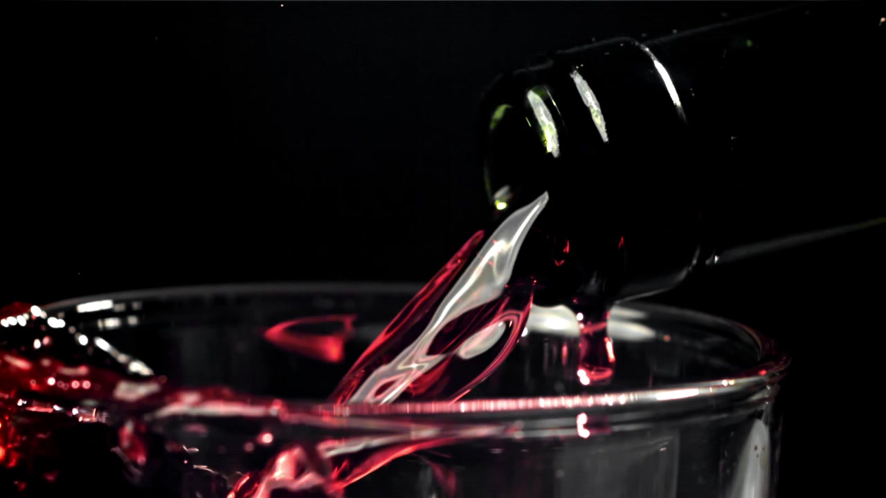 Vino tinto sirviéndose de la botella en la copa a cámara lenta.