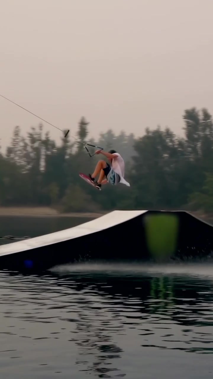 Vertical video: Cable pulling rider jumping ramp rotating riding lake with vest, board copy space