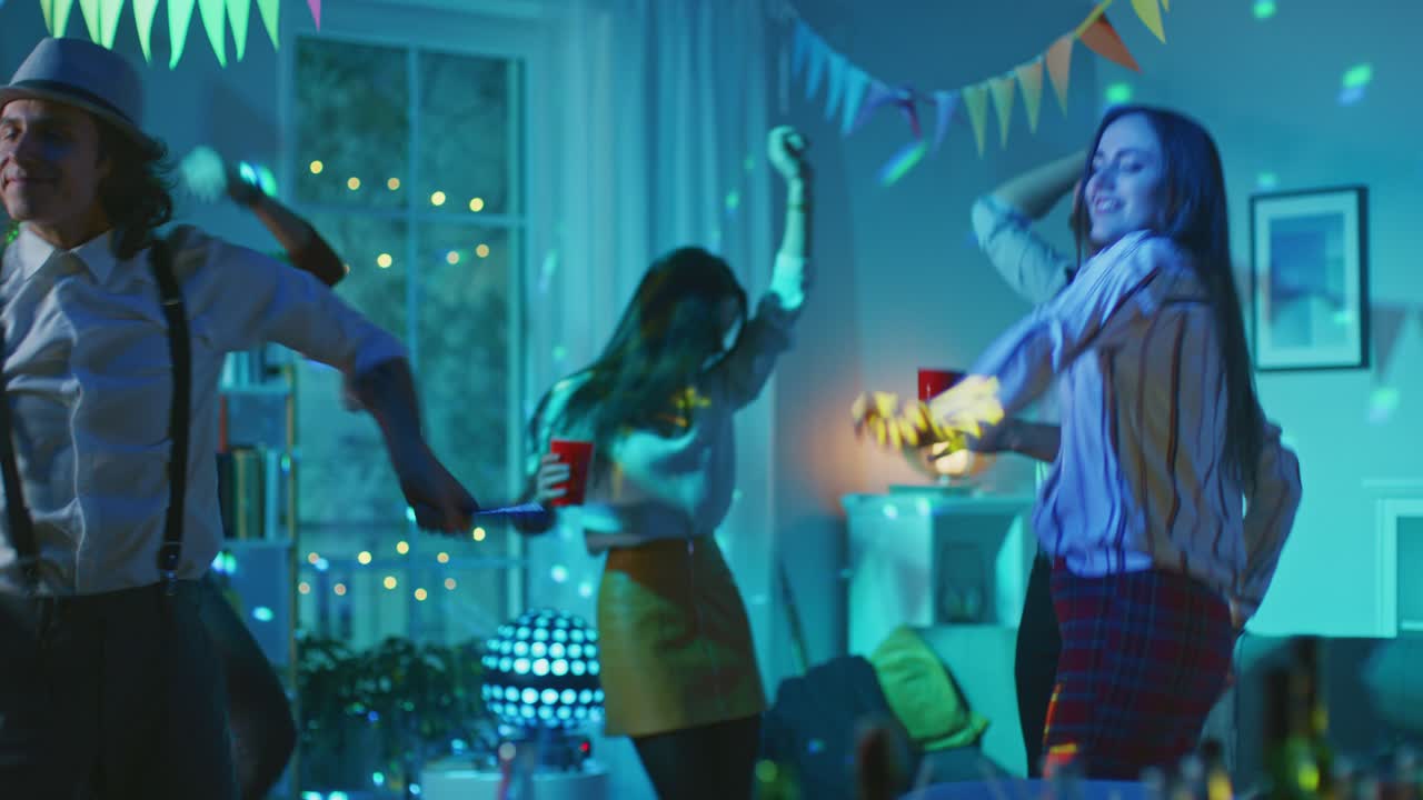 At the College House Costume Party: Diverse Group of Friends Have Fun, Dancing, Jumping, Socializing and Drinking. Stylish Boys and Girls Dance in the Living Room. Disco Neon Lights Illuminating Room.
