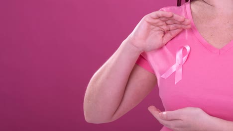 Video-of-midsection-of-caucasian-woman-wearing-pink-cancer-awareness-ribbon,-with-pink-background