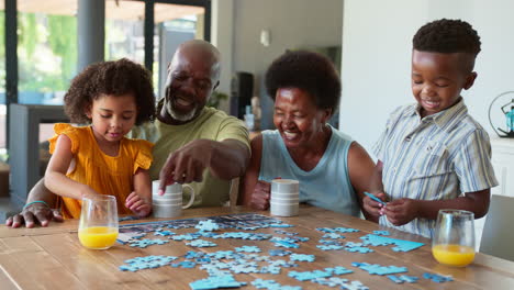 family shot with grandparents and grandchildren doing jigsaw puzzle on table at home