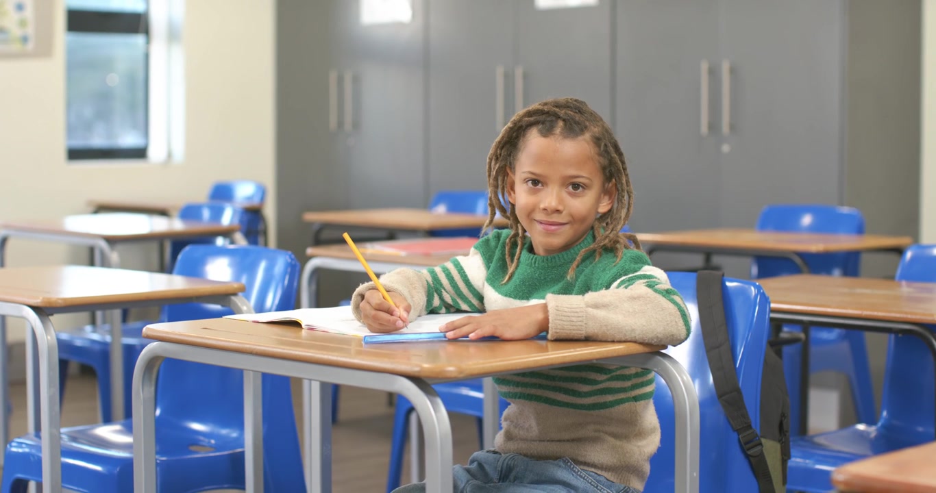 Scolaro afroamericano che scrive con la matita al banco in classe, risponde al quaderno di esercizi e sorride