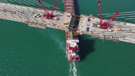 cargo vessel passing under incomplete gordie howe bridge during construction