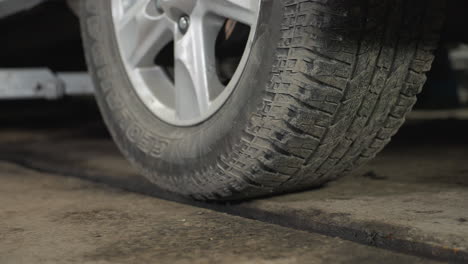 close-up of car tires and rims being lowered on a lift, rubbing against mud, highlighting the gritty details of vehicle maintenance in an auto repair shop