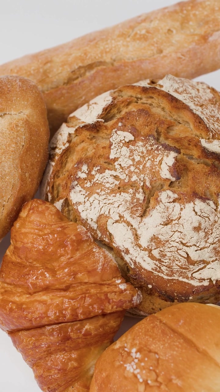 Close-up panning shot of artisan sourdough, baguettes, and croissants on a clean white surface.
