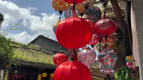 lanterns hanging outside a shop blowing in the breeze with a temple roof and blue sky in the background in hoi an, vietnam ancient town