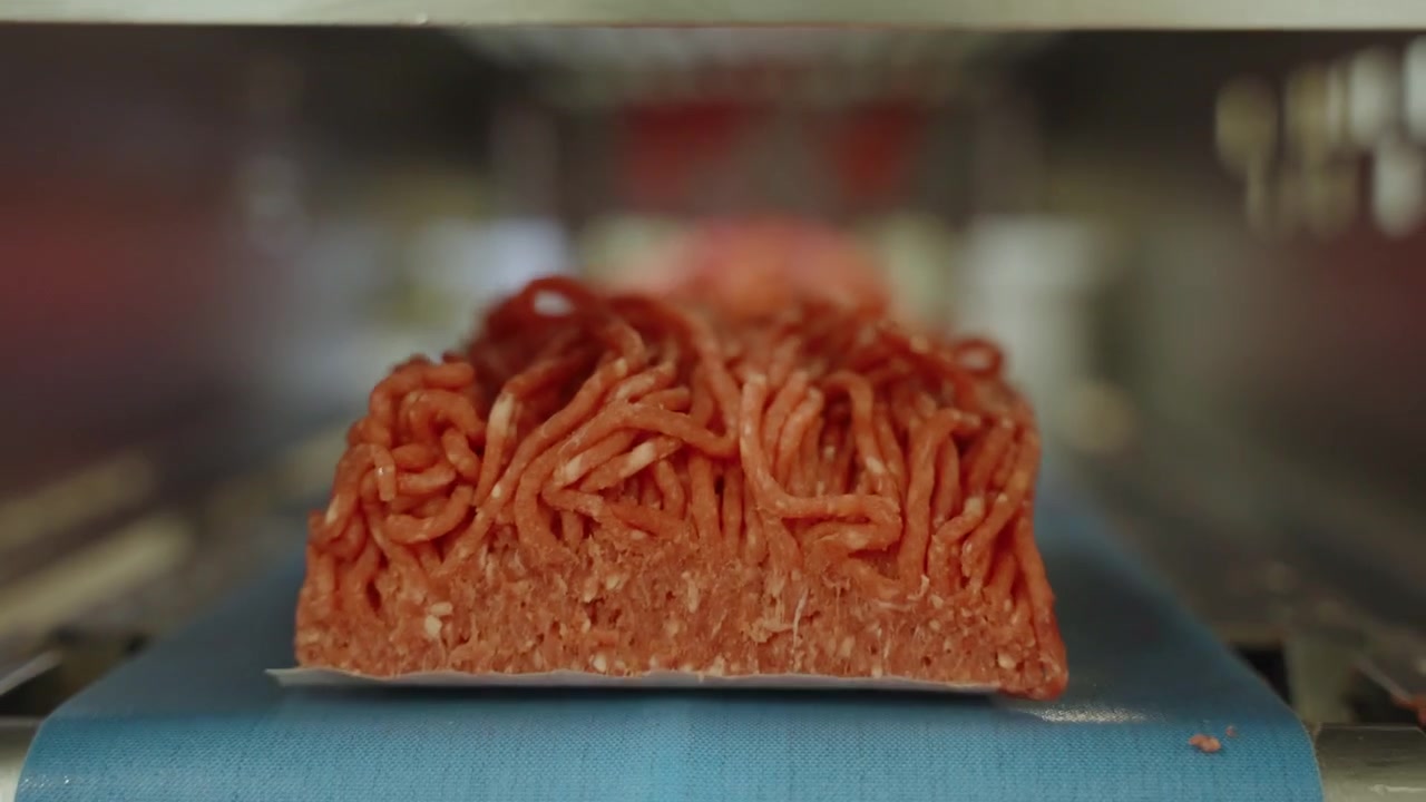 Packaged portions of minced beef ride a blue belt through a stainless steel packing tunnel in a South African meat facility.