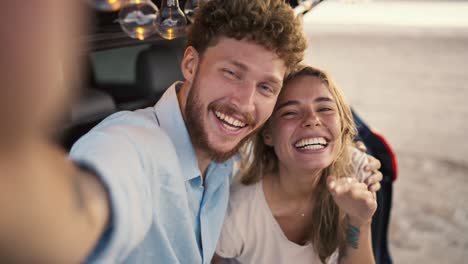 pov: a bearded guy with curly hair in a blue shirt is smiling at the camera with his blonde girlfriend while waving takes a