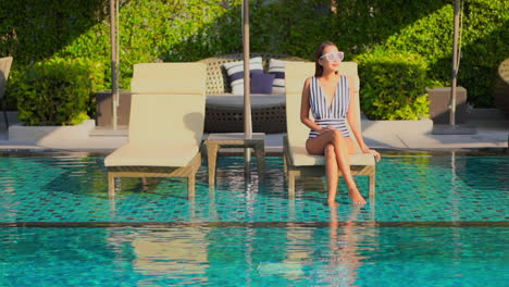 Woman-with-striped-black-and-white-swimsuit-sitting-on-deckchair-in-pool-water