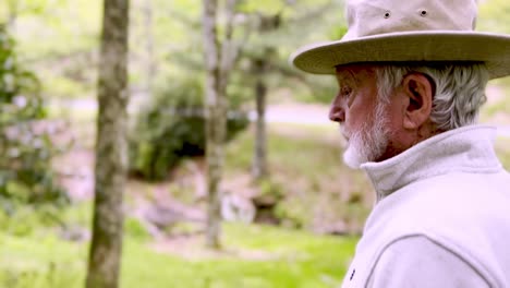 old man with hat walks down wooded trail in garden setting