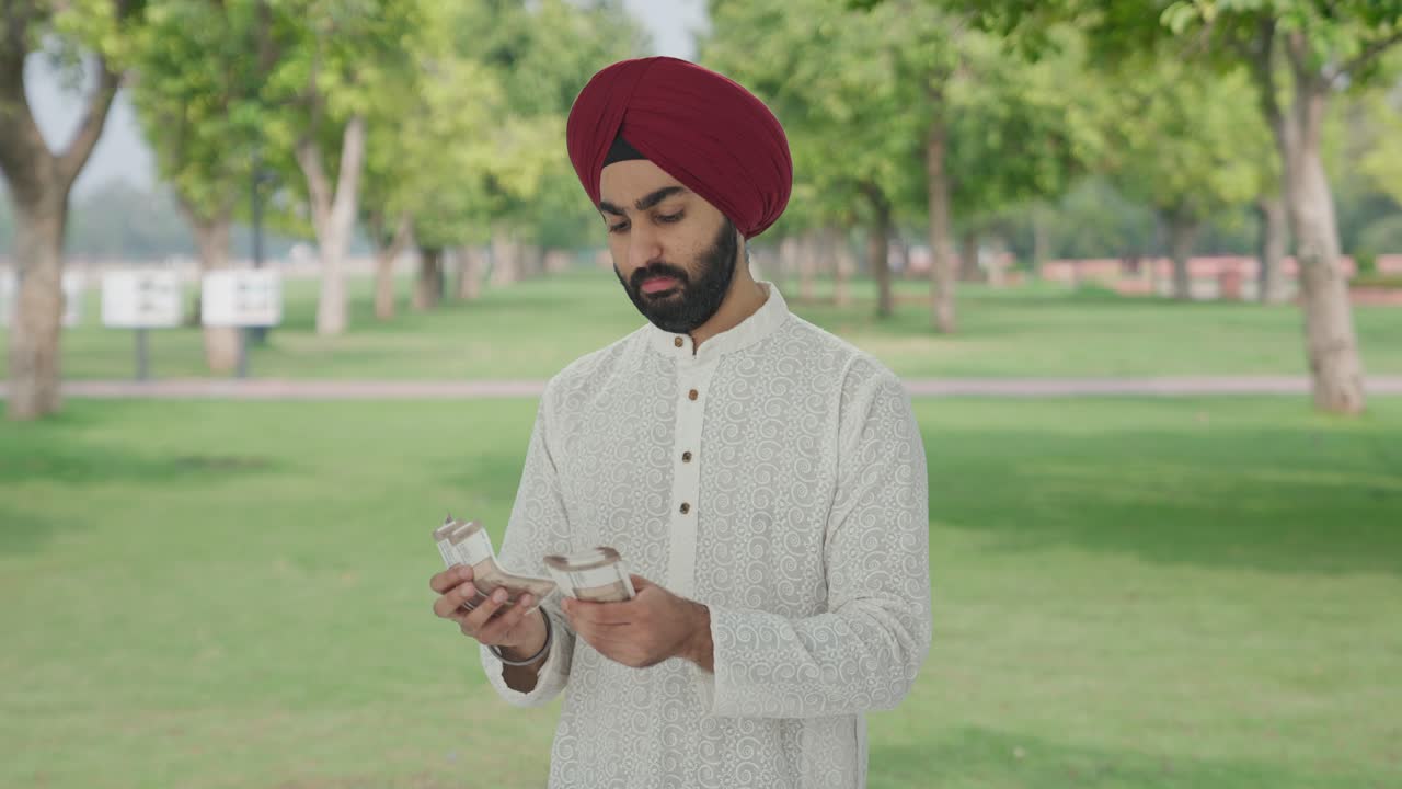 Uomo indiano Sikh che conta denaro al parco