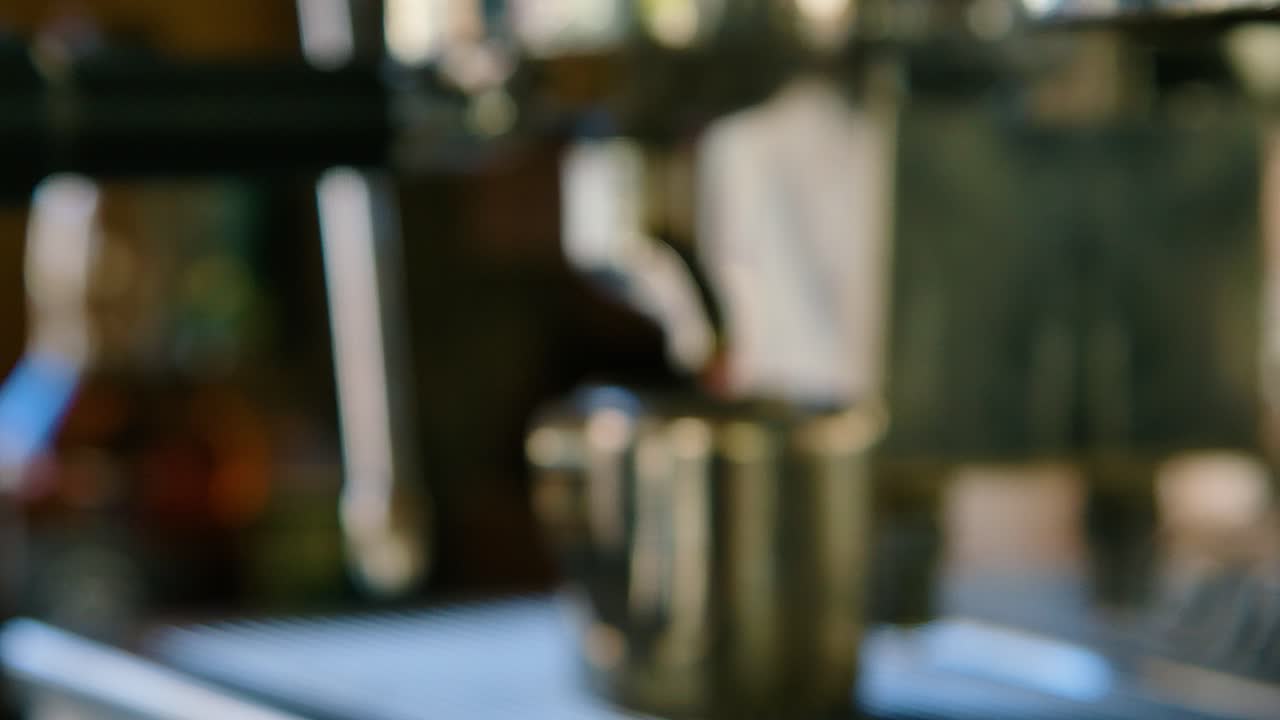 Push in to nozzle as coffee finishes dripping into metal cup, hand pulls it away, shallow depth of field