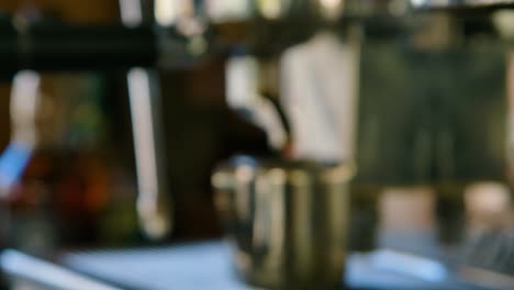 push in to nozzle as coffee finishes dripping into metal cup, hand pulls it away, shallow depth of field