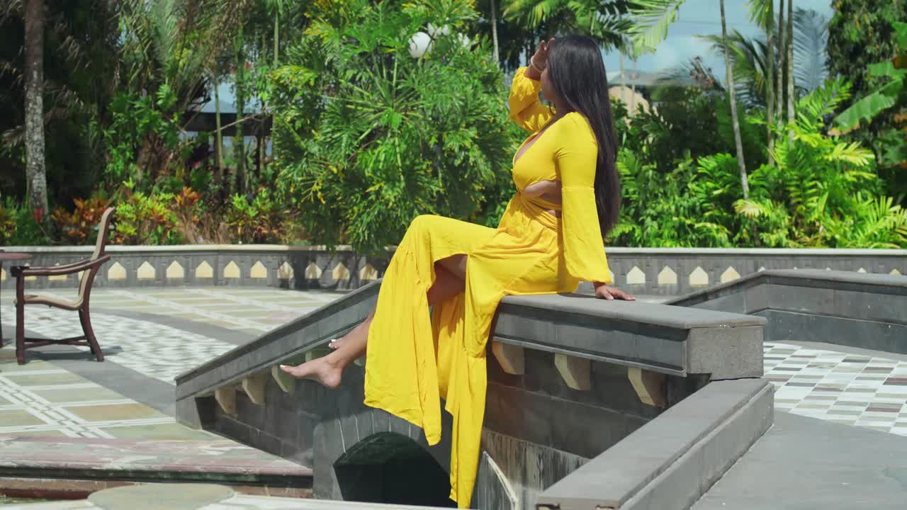 A girl in a buttery yellow dress sitting on the bridge at the grand entrance of a timeless castle.