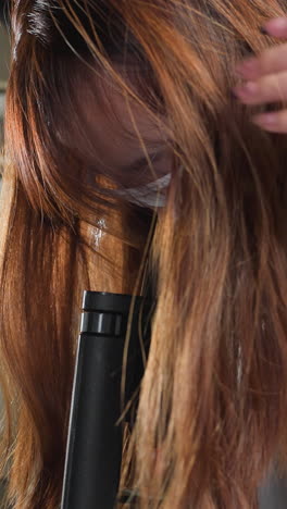 estudiante ajusta el cabello mientras se dobla para observar a través del microscopio, el cabello en cascada sobre el hombro, luego se endereza para tocar en la tableta en el taller de automóviles con herramientas, maquinaria y luz brillante