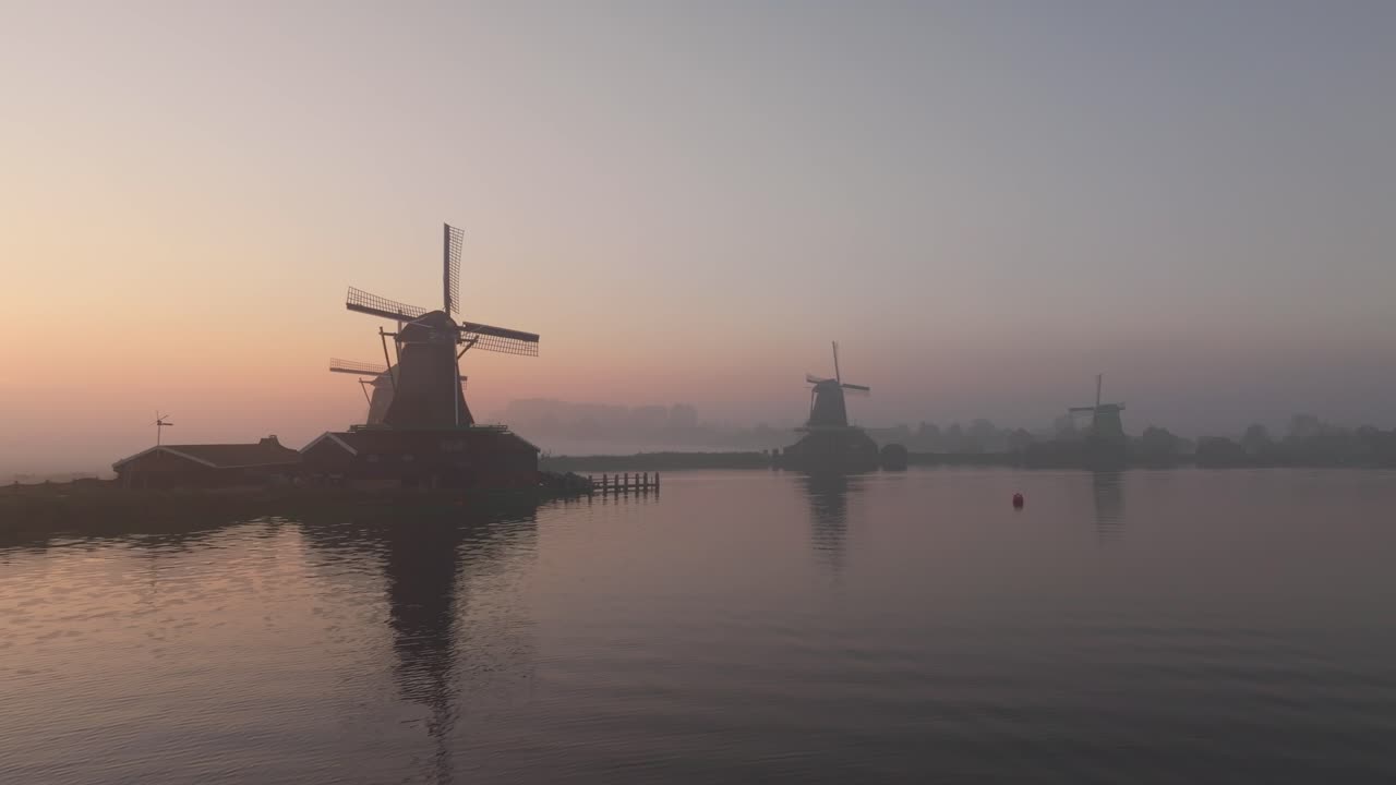 Vista aerea del famoso Zaanse Schans con mulini a vento tradizionali illuminati da una dolce alba sulla campagna olandese.