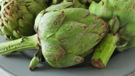 Whole-fresh-artichokes-on-plate,-rotate.-Closeup