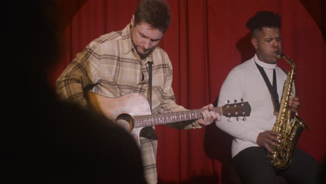 hombre latino tocando el saxo y el hombre tocando la guitarra durante la actuación de música en vivo