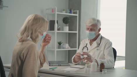 a grey haired, middle aged doctor in a facemask prescribes pills to a female patient