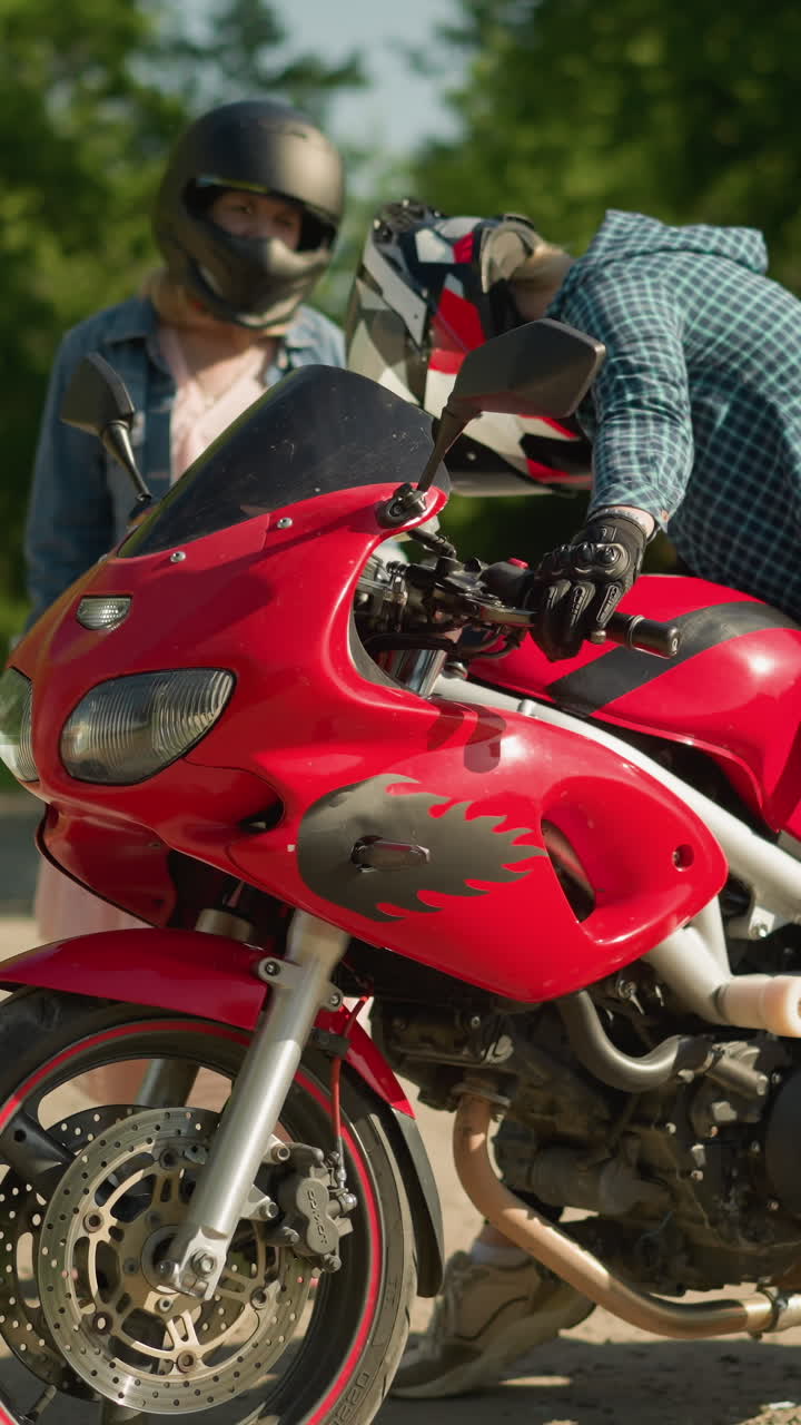 dos hermanas participan en una conversación en una carretera pavimentada rodeada de árboles, una hermana está en una bicicleta eléctrica roja, mientras que la otra, con una camisa a cuadros y pantalones negros, observa la bicicleta