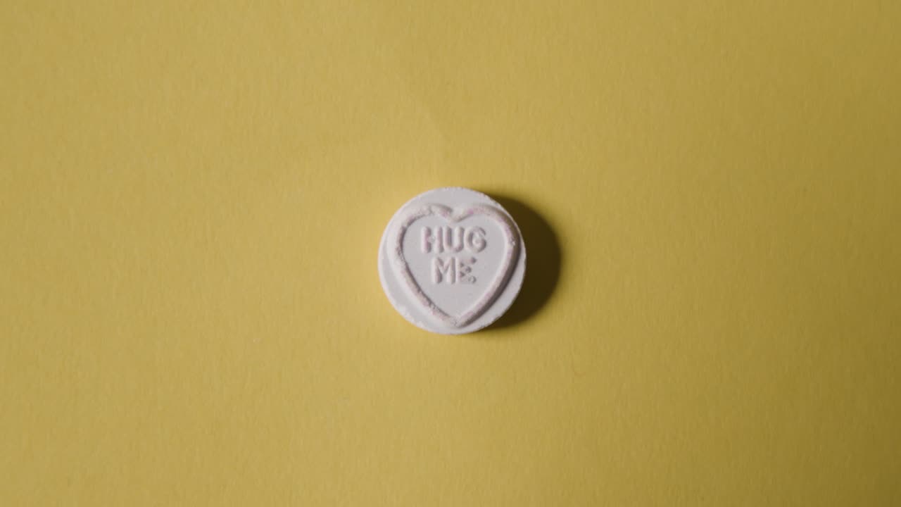 Hand Picking Up Heart Candy With Hug Me Message On Yellow Background