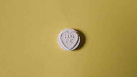 mano recogiendo caramelos de corazón con un mensaje de abrazo sobre fondo amarillo