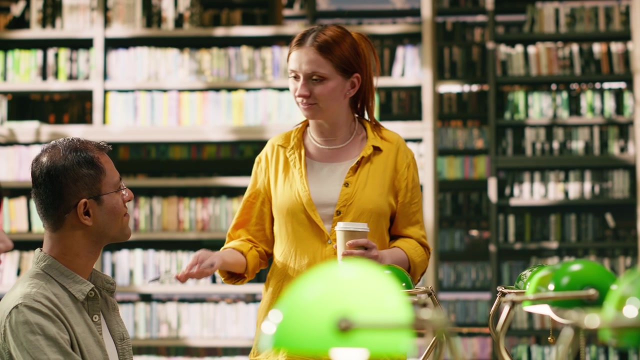Tutorin spricht mit Studierenden, die mit Büchern um einen Bibliothekstisch sitzen