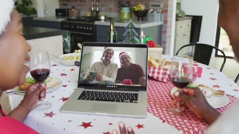 pareja afroamericana con vino usando computadora portátil para la videollamada de navidad con familia feliz en la pantalla