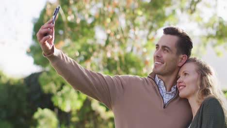 video de un feliz esposo y esposa caucásicos tomando una selfie con un teléfono inteligente en el jardín