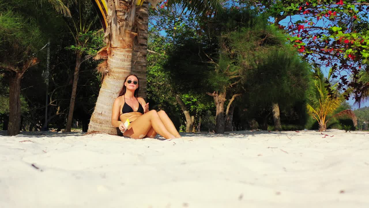 Mladá žena se opaluje a maže si tělo opalovacím krémem, chrání se tak před nebezpečným zářením tropického slunce na Bali.