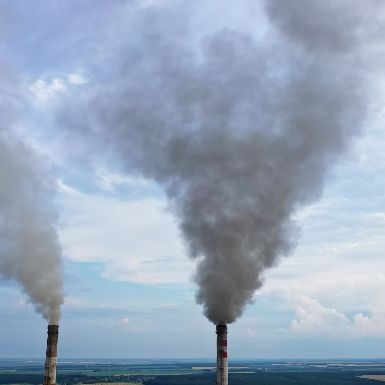 View from the drone at the old aged weathered tall industrial factory chimney with smoke over it. Cloudy sky background