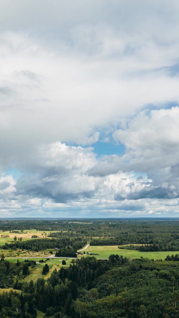 Vertical high altitude hyperlapse view of summer storm clouds developing over vast green forest and farmland. Drone view in countryside.