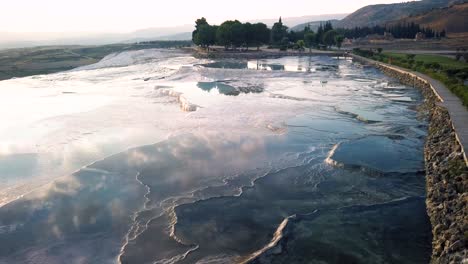 Drohnenflug-über-Pamukkale-Mit-Wunderschönen-Reflexionen-Von-Sonnenuntergang-Und-Wolken-Im-Wasser-Und-Weißen-Salzformationen,-Travertinen-Mit-Blick-Auf-Das-Tal-In-Der-Türkei