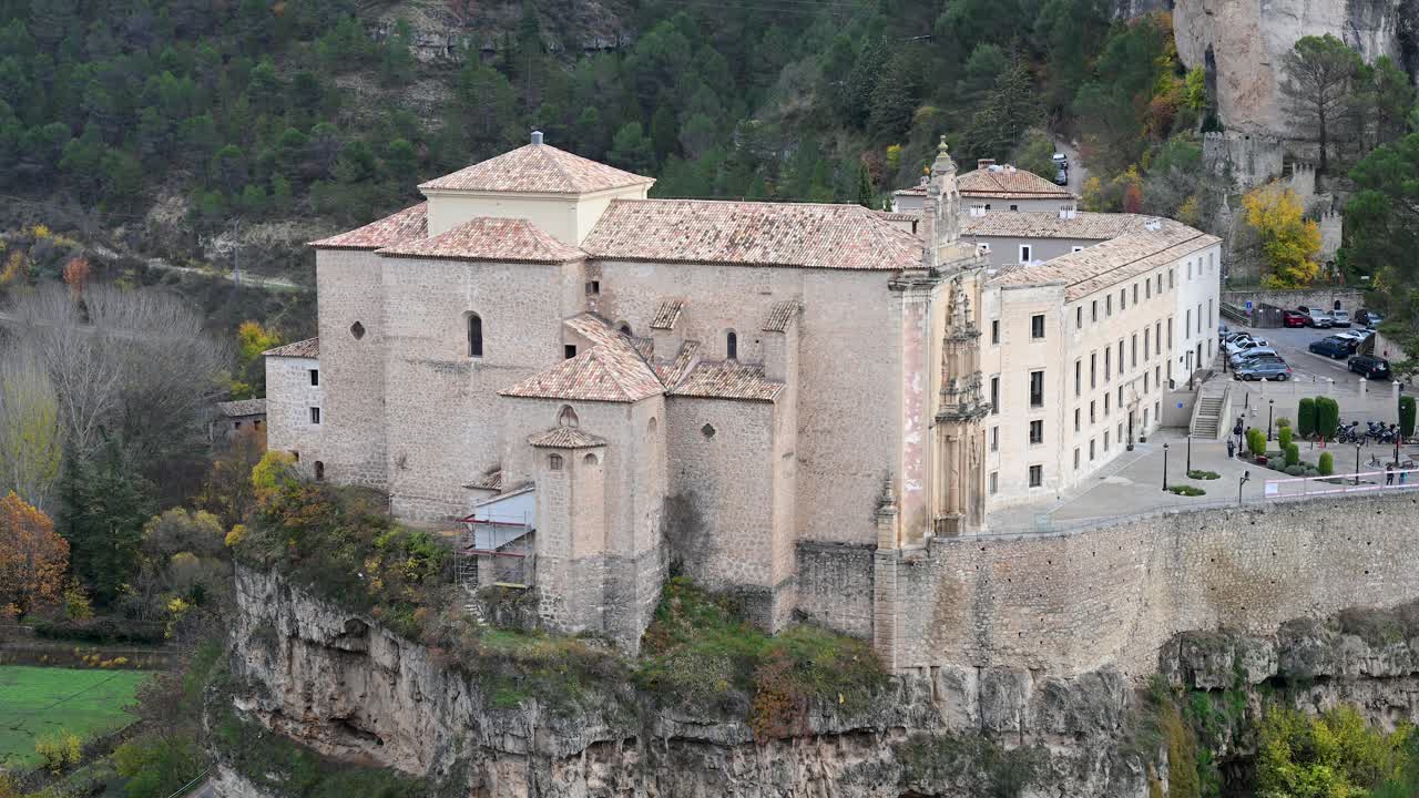 A stunning autumn landscape in Cuenca, Spain, where the historic Parador hotel emerges from a cliffside, surrounded by the rolling hills and deep gorge below.